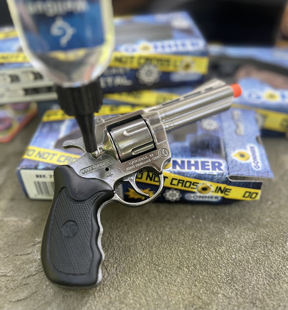 A cap gun being oiled with a bottle while resting on top of partially visible boxes of caps, highlighting maintenance for safe usage.
